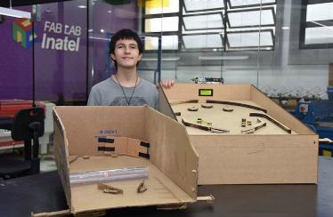 Aluno de primeiro semestre com protótipo de papelão e protótipo final desenvolvido e fabricado no Fab Lab Inatel.